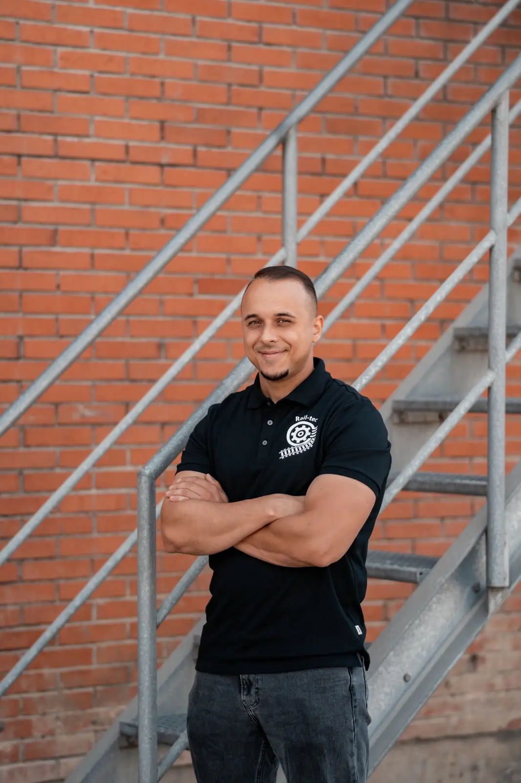 A Rail-tec member of staff in the company polo shirt, in front of a brick wall with an external staircase.